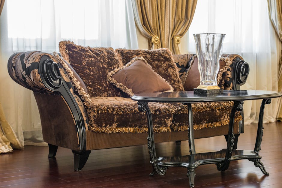 A white, tufted sofa with rolled arms and dark wooden legs positioned against a white wall with decorative paneling. The sofa's upholstery appears clean and well-maintained, set on a light hardwood fl