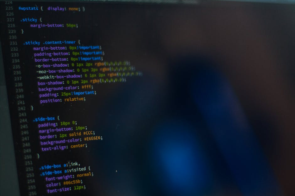 Close-up image of a computer screen displaying colorful lines of programming code with syntax highlighting, including keywords, variables, and functions, on a beige background. The screen shows a soft